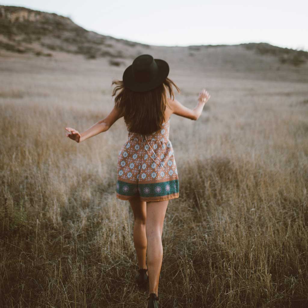 Photo behind a healthy woman walking through long grass with her arms swinging.